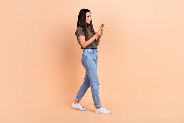 Full length body photo of young charming optimistic woman wear khaki t-shirt jeans write text for blog isolated on beige color background. - Φωτογραφία, εικόνα
