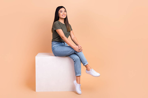 Full length cadre of dreamy cute satisfied korean model sitting wihte platform new brand purchase promo isolated on beige color background. - Valokuva, kuva