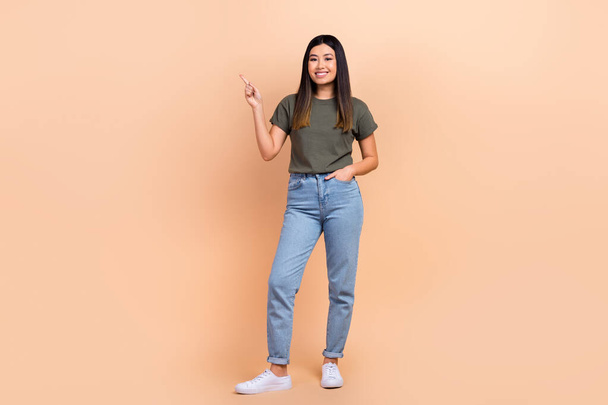 Full body photo of korean girl wear casual outfit jeans khaki t-shirt point finger mockup brand store isolated on beige color background. - Fotografie, Obrázek