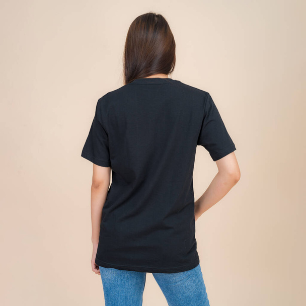 Female fashion model in black t-shirt and jeans standing in studio on beige background, trendy clothing style, copy space - Foto, Bild