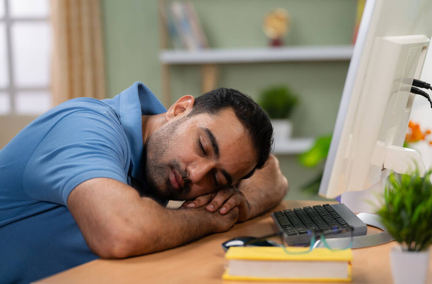 自宅でコンピュータテーブルの上で寝て疲れインド人男性-休息の概念,ストレス軽減と過労した専門家. - 写真・画像