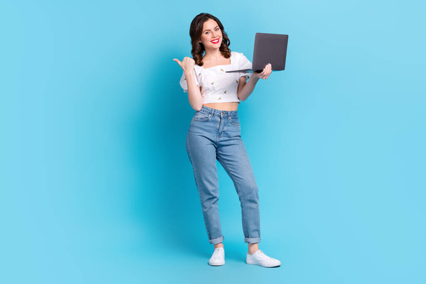 Full length photo of charming cheerful person hold netbook indicate finger empty space promo isolated on blue color background. - Фото, изображение