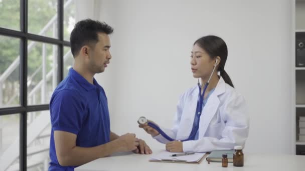 Médico revisando la frecuencia respiratoria del paciente o pulso mediante el uso de estetoscopio Paciente asiático del hombre se comprueba su salud mientras que un médico de la mujer utiliza un estetoscopio para oír la frecuencia cardíaca. - Metraje, vídeo