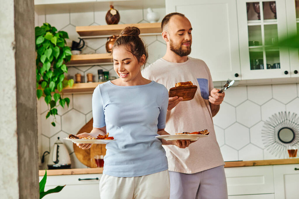 Positive woman holding breakfast near boyfriend with cutlery and bread at home in morning - Photo, Image