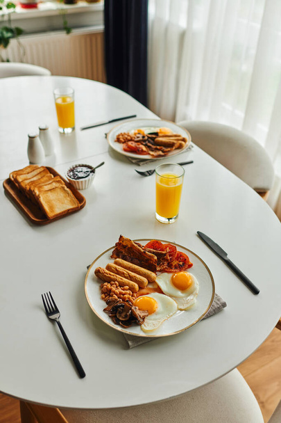 自宅でカトラリーやオレンジジュースに近い揚げ卵とソーセージの朝食のハイアングルビュー - 写真・画像