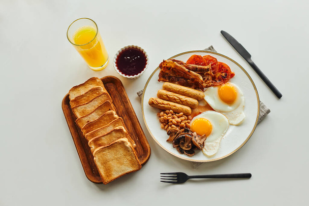 Top view of tasty breakfast with fried eggs,sausages and toasts near orange juice and jam on table - Фото, зображення