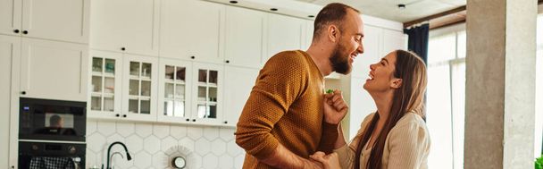 Vista lateral do casal positivo de mãos dadas enquanto dança na sala de estar em casa, banner - Foto, Imagem
