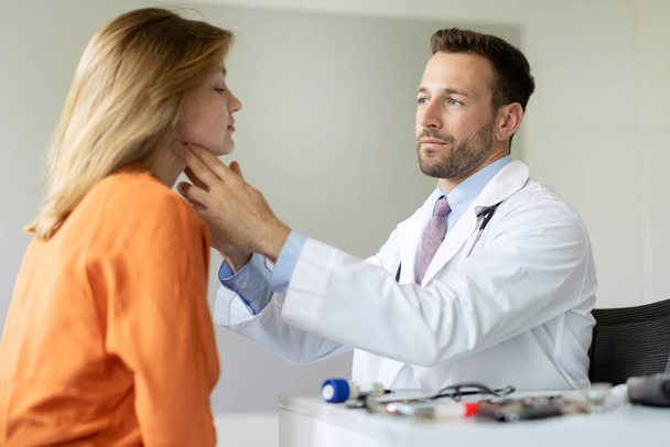 Médecin professionnel examinant la glande thyroïde de la patiente pendant le check-up dans une clinique privée, assis au bureau de l'hôpital - Photo, image