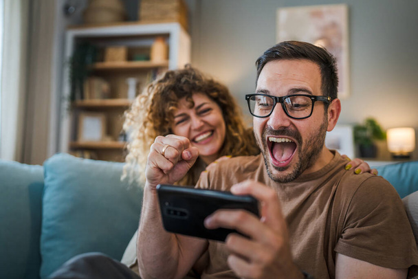 Aikuinen pari mies ja nainen valkoihoinen aviomies ja vaimo tai poikaystävä ja tyttöystävä hän pelaa videopelejä kotona pidä matkapuhelin älypuhelin hauskaa vapaa-ajan iloa ja liimaus käsite kopioi tilaa - Valokuva, kuva