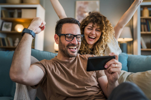Aikuinen pari mies ja nainen valkoihoinen aviomies ja vaimo tai poikaystävä ja tyttöystävä hän pelaa videopelejä kotona pidä matkapuhelin älypuhelin hauskaa vapaa-ajan iloa ja liimaus käsite kopioi tilaa - Valokuva, kuva