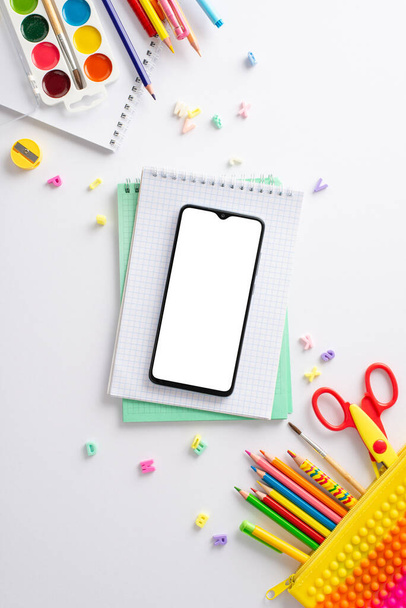 Explore the wonders of early education with this top-down vertical perspective: a captivating arrangement of child stationery on a white backdrop, offering blank notepad page for text or advertising - Foto, Imagen