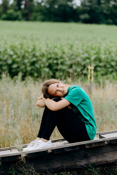 beautiful young woman with blond hair sits with her legs tucked under her.girl sits in a field.loneliness and melancholy.a feeling of peace and pleasure.alone with nature.relaxation and rest.tender. - Фото, изображение