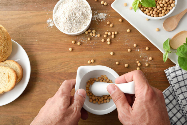 家で臼と杵で大豆粉を作り、木製のテーブルの上で大豆を乾燥させる人。トップ表示. - 写真・画像