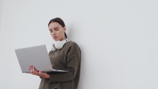 Jeune spécialiste informatique moderne debout sur fond de mur blanc travaillant sur ordinateur portable - Séquence, vidéo