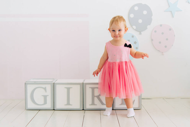 Concept of children's emotions. Portrait of lovely toddler little baby child girl with pink dress. Wooden cubes with the inscription girl. - Fotografie, Obrázek
