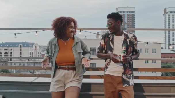 Średni strzał stylowej pary Afroamerykanów z genu Z chłodzącej się na imprezie na dachu w letni wieczór - Materiał filmowy, wideo
