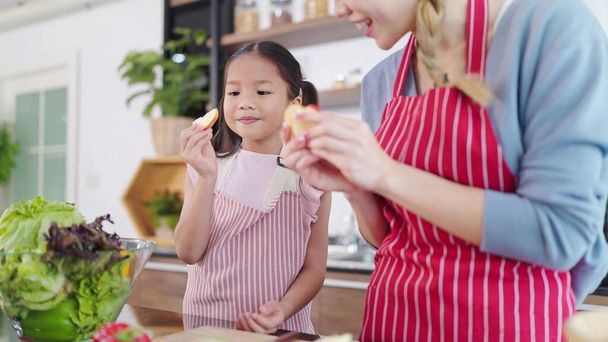 自宅のキッチンでリンゴを手に持って幸せな小さなアジアの女の子。健康管理のために果物を食べる。幸せなアジアの家族、健康的な食品の概念 - 写真・画像