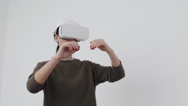Niski kąt średniego ujęcia młodej białej kobiety noszącej zestaw słuchawkowy VR w grze lub pracy, białe tło ściany - Materiał filmowy, wideo