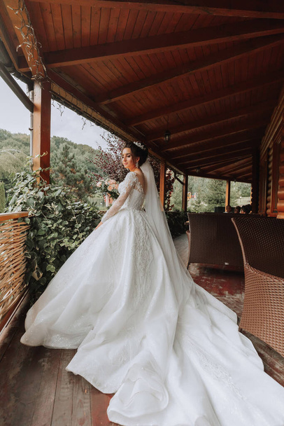 The bride in a white dress with a long train on a wooden gazebo - Foto, imagen