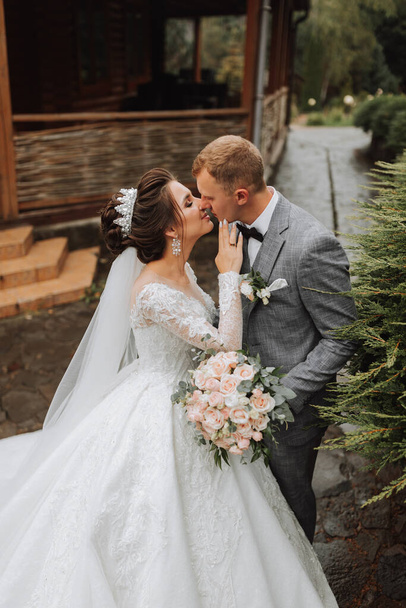 Handsome groom and charming bride together in the park. Portrait. Luxurious dress with a long train. Elegant young groom. Wedding bouquet. luxury wedding - Foto, afbeelding