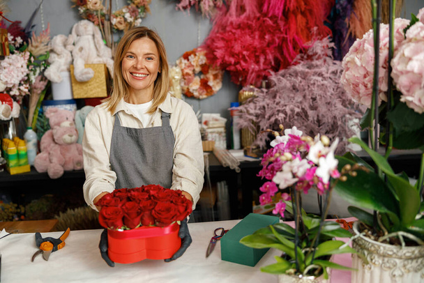 Woman florist flower shop owner hold roses composition on store background. High quality photo - 写真・画像