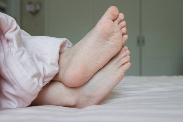 Feet under a light blanket on the bed. Concept of sleeping or waking in the morning - Foto, Imagem