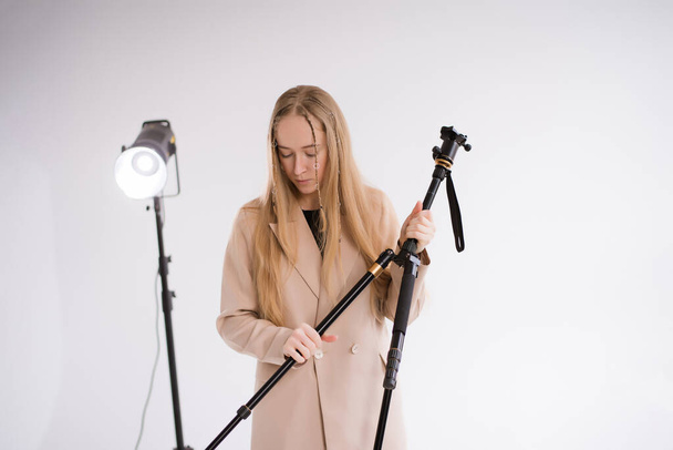 Egy női producer, videós, egy szőke, állvánnyal és fénnyel a stúdióban. Meztelen nadrágkosztüm viselése fehér alapon - Fotó, kép
