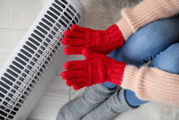 Femme se réchauffant les mains dans des gants près du radiateur à la maison, gros plan - Photo, image