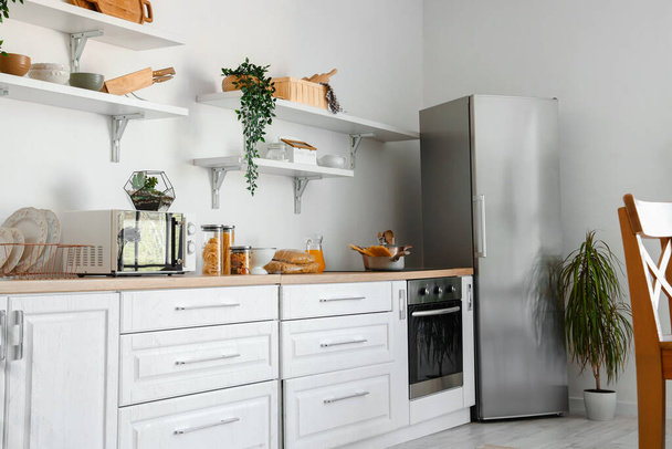 Interieur van lichte keuken met stijlvolle koelkast, aanrecht en planken - Foto, afbeelding