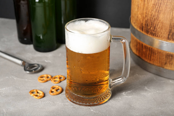 Кружка холодного пива, деревянная бочка и крендельки на столе, крупный план - Фото, изображение