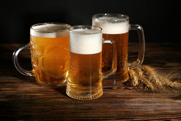 Κούπες κρύας μπύρας και πινέζες σε ξύλινο τραπέζι - Φωτογραφία, εικόνα