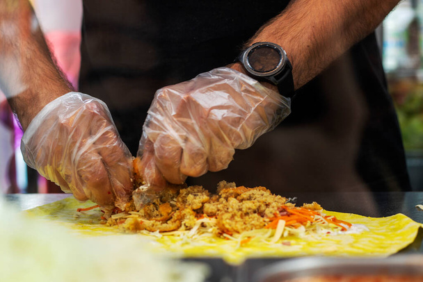 Мужские руки в одноразовых перчатках готовят вегетарианскую шаурму. уличная еда - Фото, изображение