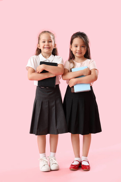 Little schoolgirls with books on pink background - Фото, изображение