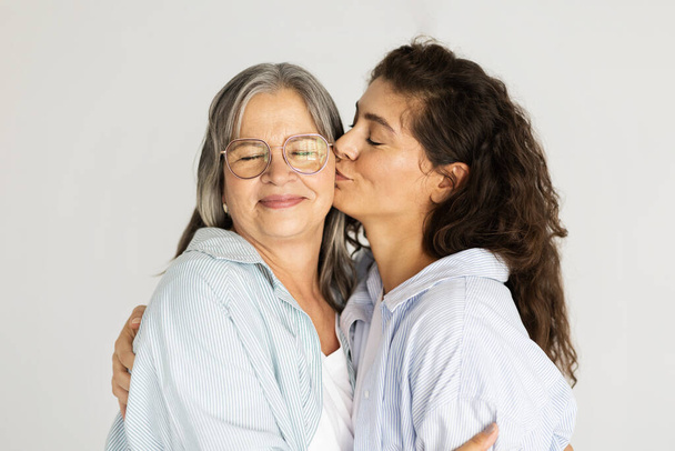 Cheerful mature woman hugging and kissing on cheek of old lady, enjoy mom daughter visit, isolated on white studio background. Family love, female generation, relationship and lifestyle - Zdjęcie, obraz
