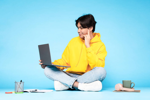 Eラーニング・レジャー。ノートパソコンを使った日本人学生が自宅で仕事をしたり、ブルースタジオを背景に床に座ってオンラインでビデオ通話をする。インターネットと教育 - 写真・画像