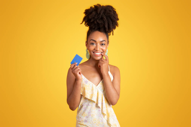 Mosolygó millenniumi afro-amerikai hölgy mutatja hitelkártya, azt javasolja, pénzügyi megtakarítások, elszigetelt sárga alapon, stúdió. Vásárlás, reklám és ajánlat, pénz ellenőrzés, fizetés, vásárlás - Fotó, kép