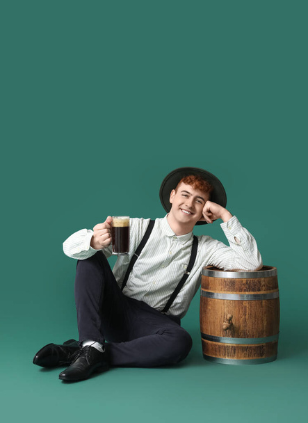 Νεαρός άνδρας με παραδοσιακά γερμανικά ρούχα με μπύρα κάθεται σε πράσινο φόντο - Φωτογραφία, εικόνα