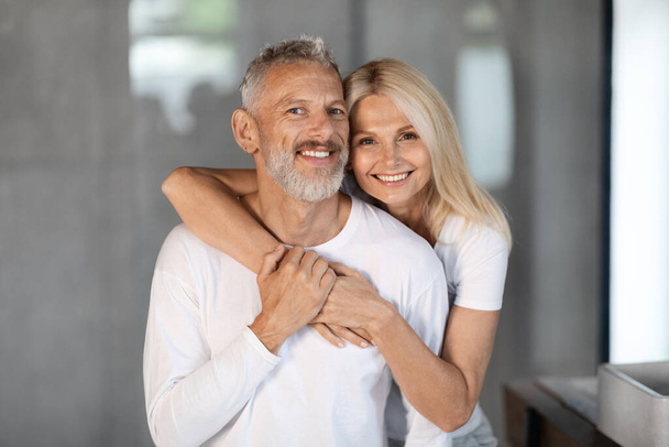 Portrait Of Happy Mature Spouses Embracing In Bathroom Interior, Loving Senior Couple Making Morning Beauty Self-Care Routine At Home, Aged Husband And Wife Smiling At Camera, Closeup Shot - 写真・画像