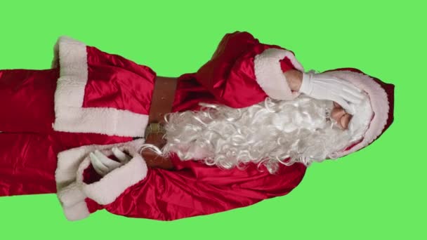 Вертикальне відео Передній вигляд батька Різдво з болючим головним болем стоїть в студії над зелено-зеленим тлом, поганий чоловік у священному червоному костюмі. Хворий святковий персонаж з відчуттям мігрені постраждав - Кадри, відео