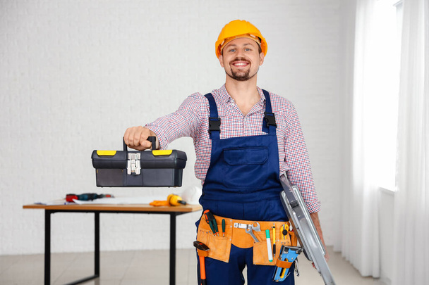 Constructor masculino con bolsa de herramientas y escalera en la habitación - Foto, Imagen
