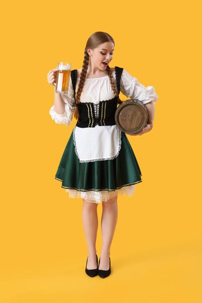 Camarera sorprendida del Octoberfest con cerveza y barril sobre fondo amarillo - Foto, imagen