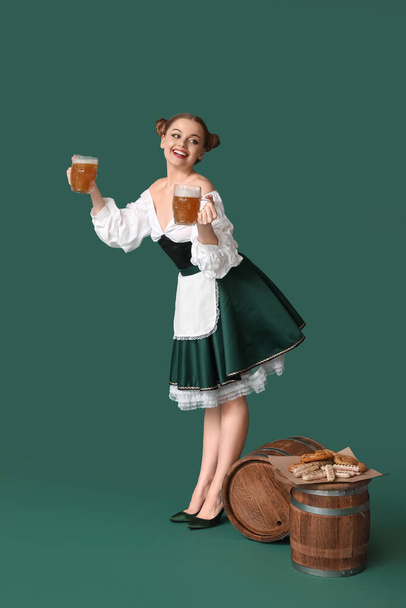 Beautiful Octoberfest waitress with beer and snacks on green background - Photo, Image