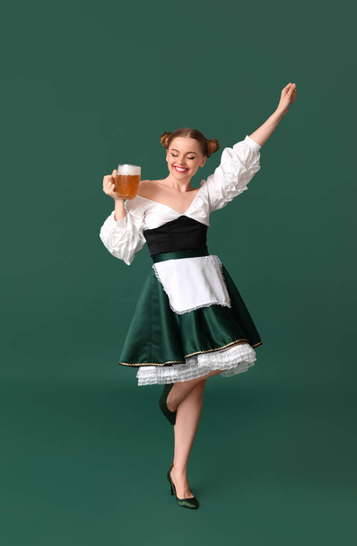 Beautiful Octoberfest waitress with beer dancing on green background - Photo, Image