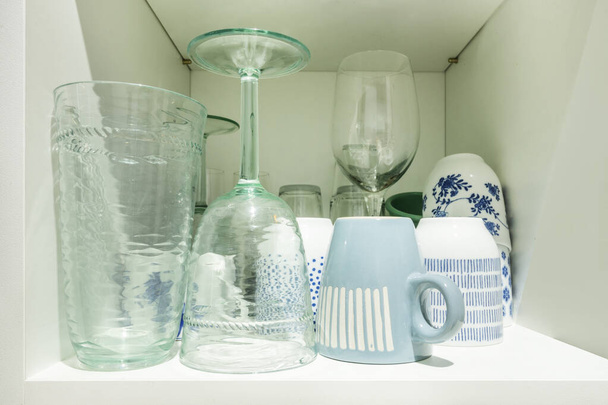 Различные изделия из стекла, хранящиеся в белом шкафу - Фото, изображение
