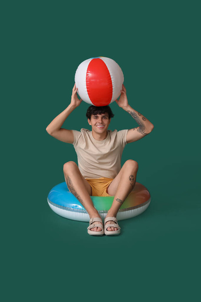 Young man with swim ring and beach ball on green background - Fotoğraf, Görsel
