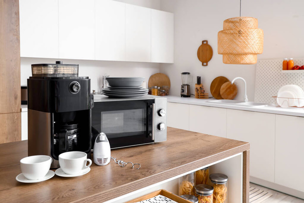 Mikrohullámú sütő, kávéfőző, keverő és tányérkészlet fa asztalra a modern konyhában - Fotó, kép