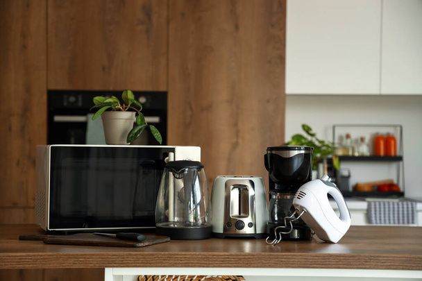Horno microondas, hervidor eléctrico, tostadora, cafetera y batidora sobre mesa de madera en cocina - Foto, Imagen