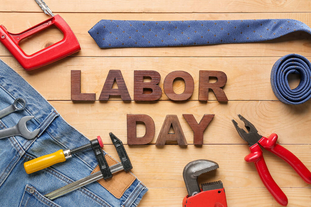 Composition with text LABOR DAY, different tools, jeans and tie on wooden background - Photo, Image