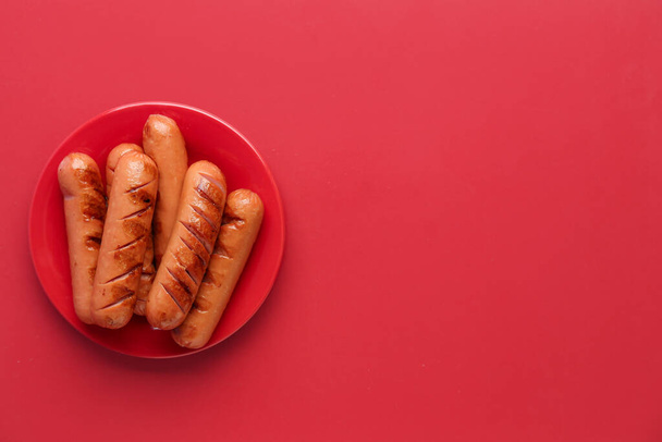 Plate with tasty grilled sausages on red background - Фото, зображення