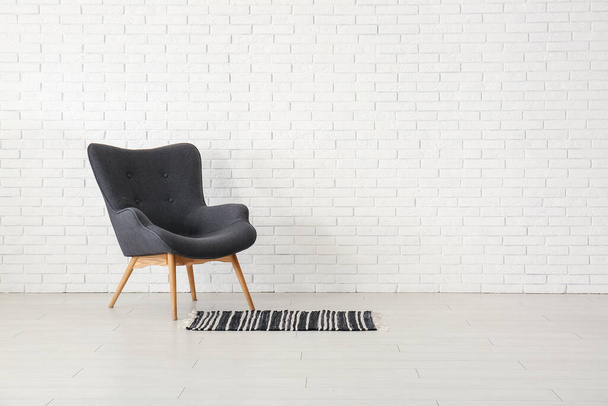 Стильне чорне крісло і килим біля білої цегляної стіни - Фото, зображення